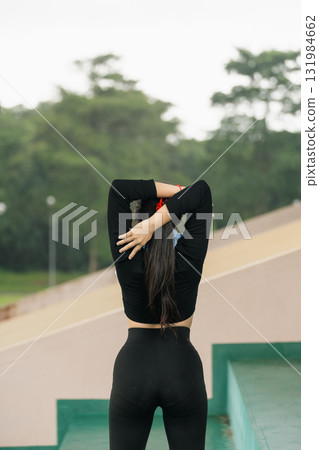Woman in Black Athletic Wear Stretching on Sports Field with Lush Green Background and Calm Atmosphere for Fitness and Wellness Themes 131984662