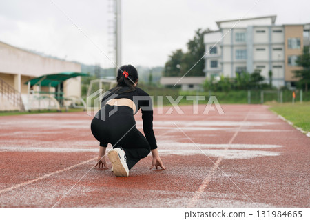 Female Athlete Preparing for Race on Track at Outdoor Stadium, Focus on Sprinting Posture with Determined Expression and Training Environment Female Athlete Preparing for Race on Track at Outdoor Stadium, Focus on Sprinting Posture with Determined Expression and Training Environment 131984665
