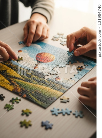 Close-up of hands assembling a jigsaw puzzle on a wooden table. People working together on a hobby. Teamwork and leisure activity concept Close-up of hands assembling a jigsaw puzzle on a wooden table. People working together on a hobby. Teamwork and leisure activity concept 131984740