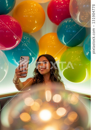 Young Hispanic woman taking a selfie with a smartphone. Smiling female in a vibrant, colorful balloon-decorated setting. Modern lifestyle and social media concept 131984778