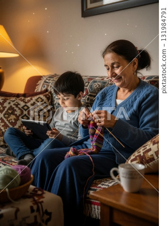 A grandmother knitting on a couch while her grandson uses a digital tablet. Intergenerational family bonding with traditional hobbies and modern technology. Cozy home lifestyle concept A grandmother knitting on a couch while her grandson uses a digital tablet. Intergenerational family bonding with traditional hobbies and modern technology. Cozy home lifestyle concept 131984791