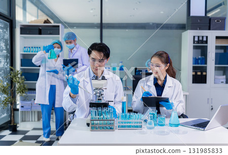 Team of biochemical research scientists working with a microscope for vaccine development Team of biochemical research scientists working with a microscope for vaccine development 131985833