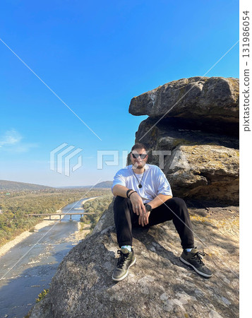 Man Sitting on Cliff Overlooking River and Valley Man Sitting on Cliff Overlooking River and Valley 131986054