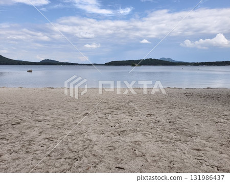 Enjoy a picturesque view of a serene lake, featuring a sandy beach beneath a bright blue sky 131986437