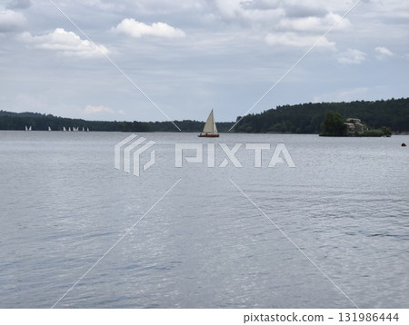 Sailboat Gliding Across a Tranquil Lake Surrounded by a Beautiful Scenic Landscape Sailboat Gliding Across a Tranquil Lake Surrounded by a Beautiful Scenic Landscape 131986444