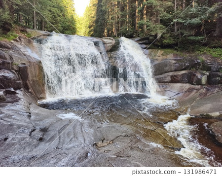 A beautiful and serene waterfall gracefully cascading in a lush forest landscape A beautiful and serene waterfall gracefully cascading in a lush forest landscape 131986471