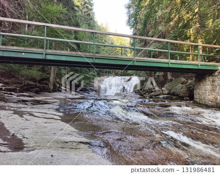 A Serene Bridge that Spans Over a Tranquil Waterfall Surrounded by a Lush Forest Area 131986481