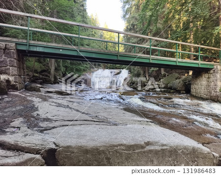 A Tranquil Bridge Stretching Over a Serene Waterfall Nestled in a Lush, Green Forest 131986483
