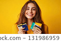 Smiling Caucasian woman in yellow winter sweater holding credit card for shopping isolated on bright yellow background 131986959
