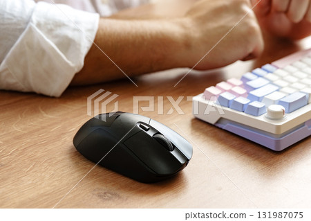 Close-up of a computer mouse next to a colorful mechanical keyboard on a wooden desk 131987075