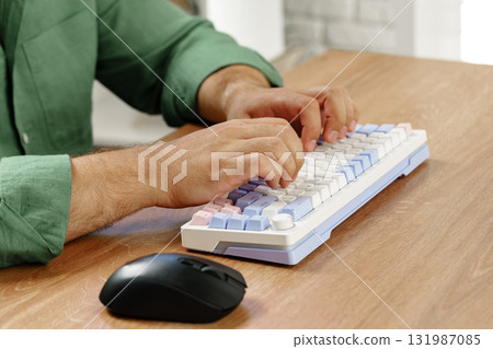 Hands typing on a pastel colored keyboard beside a black mouse in a cozy workspace Hands typing on a pastel colored keyboard beside a black mouse in a cozy workspace 131987085