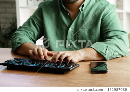 Person typing on keyboard while using smartphone at home office during daytime Person typing on keyboard while using smartphone at home office during daytime 131987086