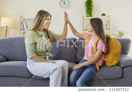 Happy mom and schoolgirl give a high five on sofa before classes, cheerful mood 131987722