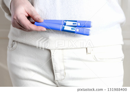 Woman in white clothes holds a blue Ozempic injection pen for diabetics and weight loss. Woman in white clothes holds a blue Ozempic injection pen for diabetics and weight loss. 131988400