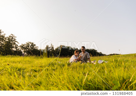 Father and son sit on a blanket in a lush green meadow, sharing stories and laughter under the warm sun, creating lasting memories in nature Father and son sit on a blanket in a lush green meadow, sharing stories and laughter under the warm sun, creating lasting memories in nature 131988405