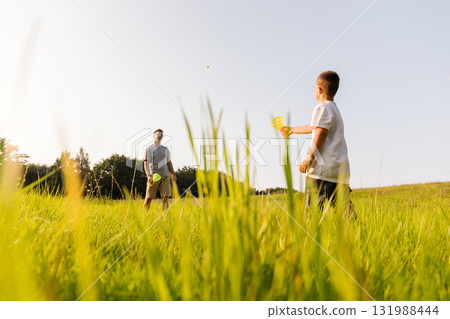 A father and son spend quality time in a green field, playing catch with bright toys under the warm sun. The joyful moments create lasting memories in nature 131988444