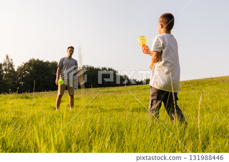 A father and his young son are having fun together in a lush green field. They are playing catch with colorful balls as the sun shines brightly on a warm afternoon A father and his young son are having fun together in a lush green field. They are playing catch with colorful balls as the sun shines brightly on a warm afternoon 131988446