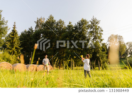 A father and his young son are having fun together in a sunny field filled with green grass and hay bales. They are smiling and playing catch with a ball A father and his young son are having fun together in a sunny field filled with green grass and hay bales. They are smiling and playing catch with a ball 131988449