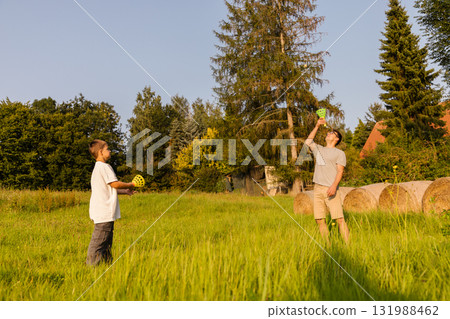 A father and son are spending quality time outdoors, playing catch with colorful balls. It is a warm, sunny day, and they are surrounded by lush greenery and hay bales A father and son are spending quality time outdoors, playing catch with colorful balls. It is a warm, sunny day, and they are surrounded by lush greenery and hay bales 131988462