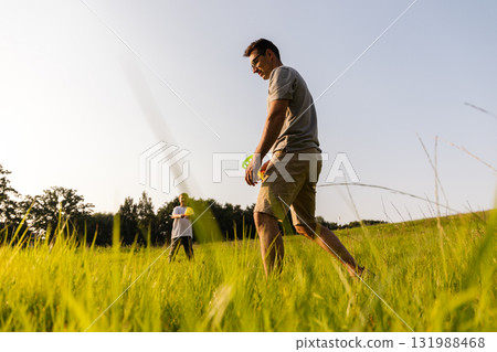 Two family members share a joyful moment outdoors. The father and son engage in playful activities in a lush green field under a clear blue sky on a sunny day Two family members share a joyful moment outdoors. The father and son engage in playful activities in a lush green field under a clear blue sky on a sunny day 131988468