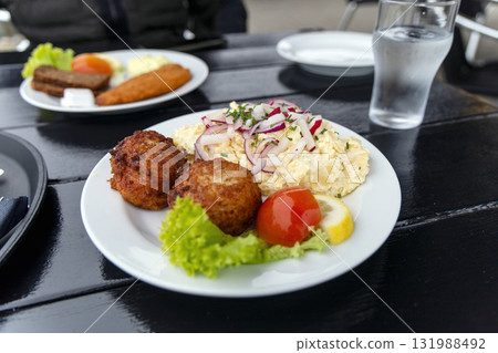 Seafood restaurant on the seashore. White plate with fish patties, fish fillets and potato salad. Seafood restaurant on the seashore. White plate with fish patties, fish fillets and potato salad. 131988492