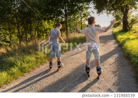 Two friends are happily inline skating along a sunlit path surrounded by trees. They are enjoying their time outdoors on a warm day, filled with laughter and friendship Two friends are happily inline skating along a sunlit path surrounded by trees. They are enjoying their time outdoors on a warm day, filled with laughter and friendship 131988539