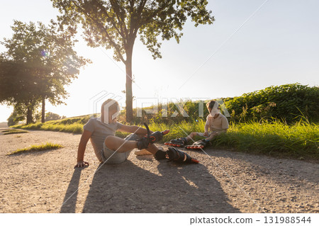 Two friends are inline skating in a sunny park. They are having fun spending their free time outdoors, enjoying each other's company and the fresh air 131988544