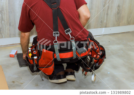 Electrical kneels on floor, using various tools in building space during works day 131989802