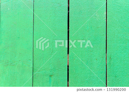 Green painted wooden fence with visible vertical planks and natural wood texture. Surface shows rough grain patterns, small cracks, and gaps between boards, creating rustic outdoor background Green painted wooden fence with visible vertical planks and natural wood texture. Surface shows rough grain patterns, small cracks, and gaps between boards, creating rustic outdoor background 131990200