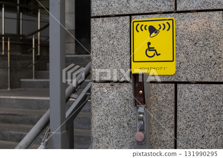 Yellow accessibility sign. Indicates call system with bell and is positioned on wall near stairs, with visible button to activate system. Offering assistance in public spaces 131990295