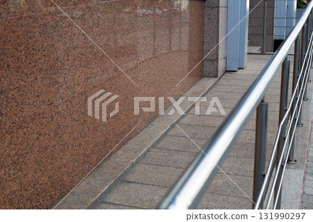 Smooth granite surface with polished finish, paired with a metallic handrail running along the pavement, showcasing modern urban design and accessibility features Smooth granite surface with polished finish, paired with a metallic handrail running along the pavement, showcasing modern urban design and accessibility features 131990297