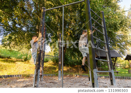 Two children are playing joyfully in a natural setting, climbing on playground equipment and enjoying the outdoors on a sunny day 131990303