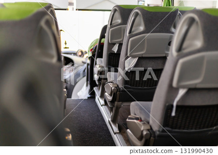Inside a bus, the scene captures empty, modern seats arranged tidily along the aisle. Bright daylight streams through the large windows, creating an inviting atmosphere Inside a bus, the scene captures empty, modern seats arranged tidily along the aisle. Bright daylight streams through the large windows, creating an inviting atmosphere 131990430