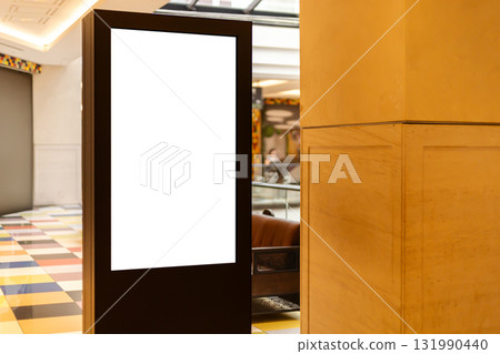 A digital display stand is positioned in a modern lobby area. The sleek design features a blank screen, offering space for advertisements 131990440