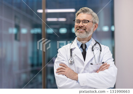 Experienced male doctor wearing a white lab coat and stethoscope, standing with arms crossed, smiling thoughtfully and looking away in a modern medical setting Experienced male doctor wearing a white lab coat and stethoscope, standing with arms crossed, smiling thoughtfully and looking away in a modern medical setting 131990663