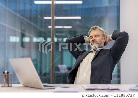 Mature businessman with gray hair and beard closing eyes and resting hands behind head, enjoying a peaceful moment of relaxation and job satisfaction at the office desk Mature businessman with gray hair and beard closing eyes and resting hands behind head, enjoying a peaceful moment of relaxation and job satisfaction at the office desk 131990727