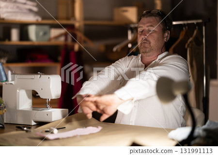 Sitting at workplace, man tailor does limbering-up, warms up numb muscles 131991113