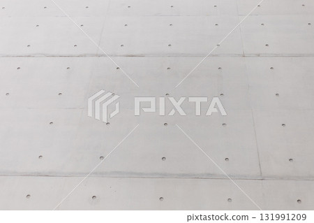 The view showcases a smooth concrete wall featuring an array of small, evenly spaced holes. The structure reflects contemporary design elements of an urban environment The view showcases a smooth concrete wall featuring an array of small, evenly spaced holes. The structure reflects contemporary design elements of an urban environment 131991209