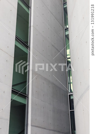 The structure showcases sleek concrete walls accented with large glass windows. Natural light filters into the interior, emphasizing the minimalist architectural design 131991218