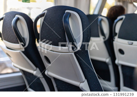 Passengers travel inside a bus, viewing the backs of comfortable seats with handles. Sunlight streams through the windows, illuminating the space and creating a welcoming atmosphere Passengers travel inside a bus, viewing the backs of comfortable seats with handles. Sunlight streams through the windows, illuminating the space and creating a welcoming atmosphere 131991239
