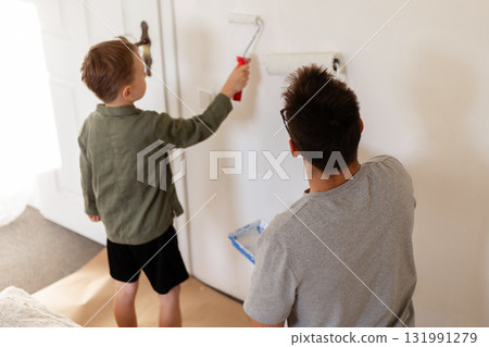 A man and his young son are painting the walls of their bedroom. They are whitewashing the walls as part of a home improvement project. The boy actively helps his father A man and his young son are painting the walls of their bedroom. They are whitewashing the walls as part of a home improvement project. The boy actively helps his father 131991279