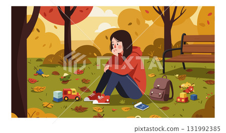 Child sitting on grass in autumn park surrounded by toys and fallen leaves in landscape 131992385