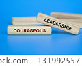 Wooden block on blue background showing COURAGEOUS LEADERSHIP text for confidence and strength 131992557
