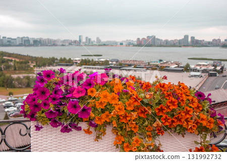 Bright yellow and red petunias in a planter in the foreground blurred view of the river embankmen 131992732