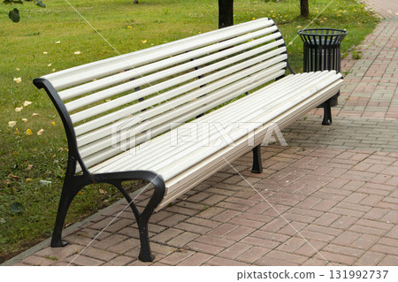 White park bench on brick walkway with trash bin White park bench on brick walkway with trash bin 131992737