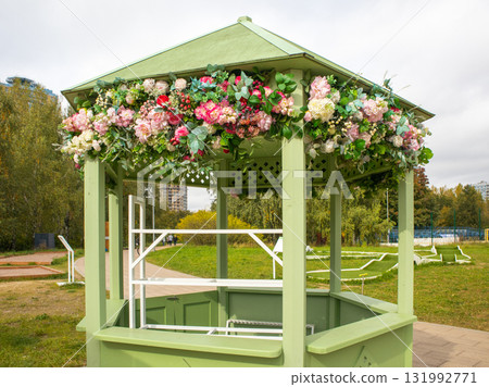 Green gazebo with pastel floral garland in park spring decor Green gazebo with pastel floral garland in park spring decor 131992771