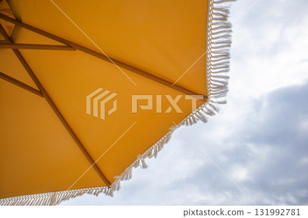 Yellow beach umbrella with fringe against cloudy sky Yellow beach umbrella with fringe against cloudy sky 131992781