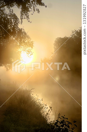 Experience the serene beauty of a stunning sunrise over a misty river landscape 131992827