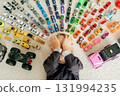 Young boy covers his face with hands while lying among toy cars on carpet playful peekaboo moment and childhood shyness 131994235
