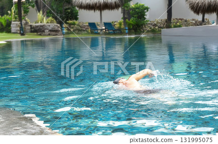 Man enjoying a relaxing, healthy swim in a beautiful pool on a sunny day. A perfect, tranquil escape for wellness and self-care. 131995075